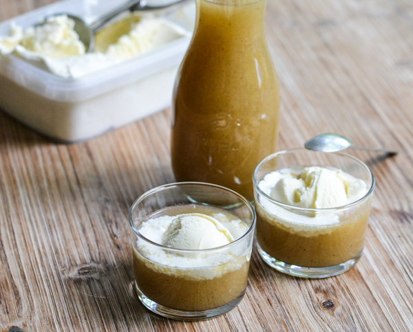 To glas med æblekompot toppet med vaniljeis og en flaske kompot ved siden af