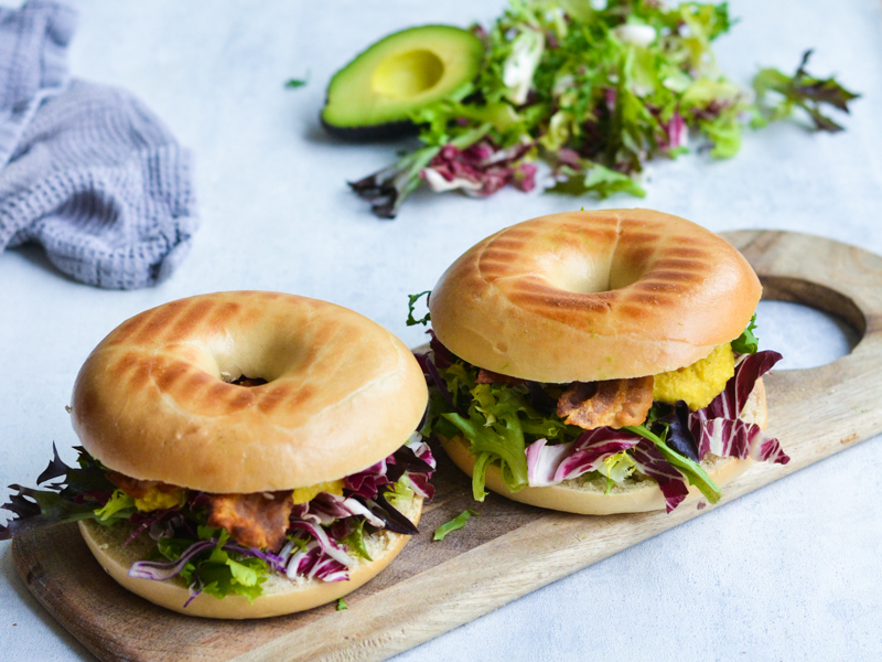 To bagels fyldt med frisk salat, bacon og avocado på skærebræt