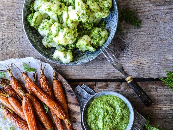 Bagte gulerødder og blomkål med grøn pesto på rustikt bord