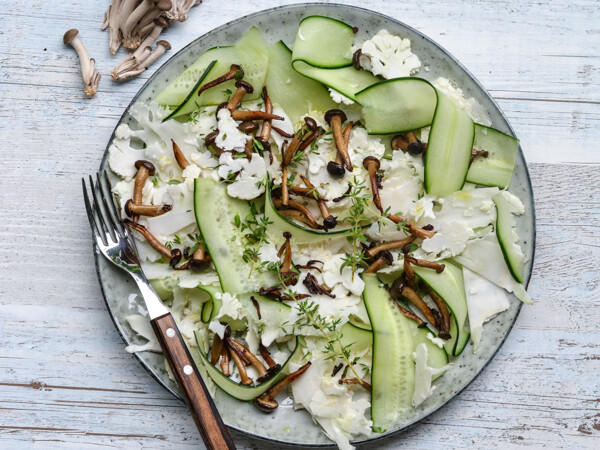 En elegant tallerken med rå svampe, tynde agurkeskiver og kål på en træbord