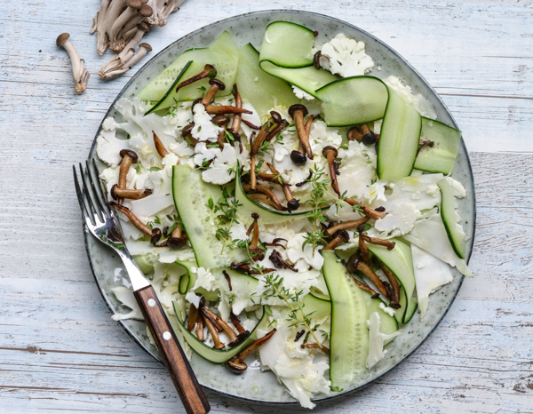 En elegant tallerken med rå svampe, tynde agurkeskiver og kål på en træbord
