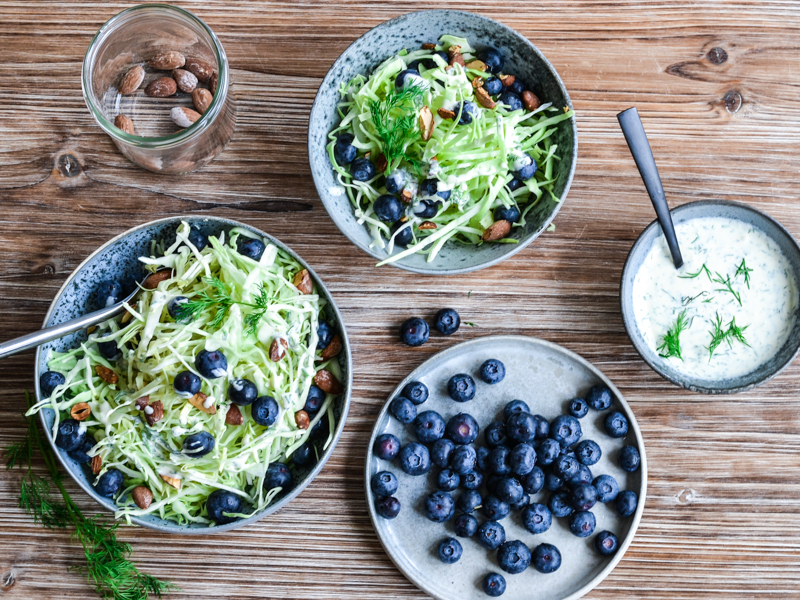 Skåle med salat, blåbær og dressing på træbord
