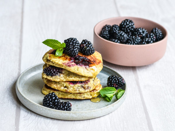 En tallerken med pandekager, brombær og mynteblade ved siden af en skål med brombær