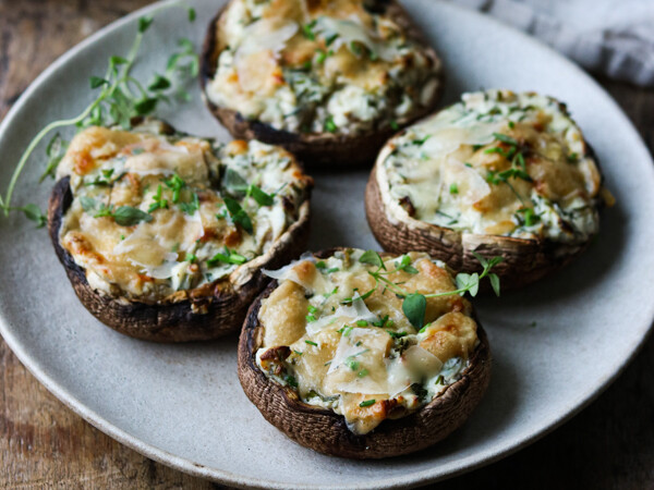Fire fyldte portobellosvampe på en beige tallerken med friske krydderurter.