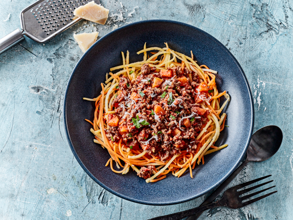 Spaghetti med kød- og tomatsauce i en blå tallerken med parmesan ved siden af