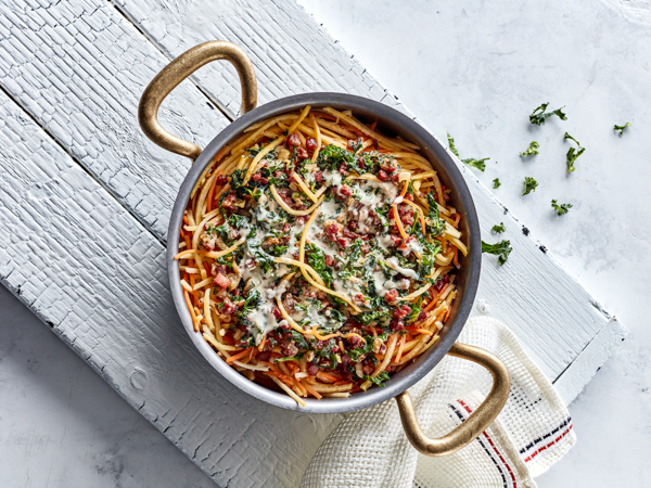 En gryde med spaghetti, kødsauce og drysset persille på hvidt bord