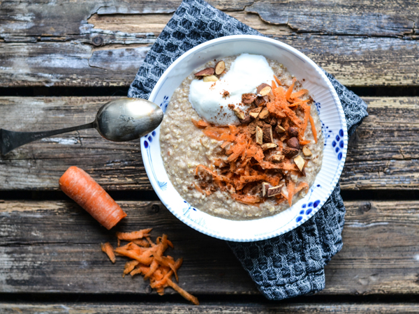 Skål med havregrød toppet med yoghurt, revet gulerod og hakkede mandler på et rustikt bord. ---