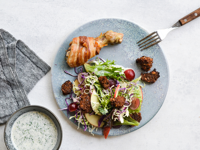 En tallerken med et kyllingelår, salat og en skål dressing ved siden af