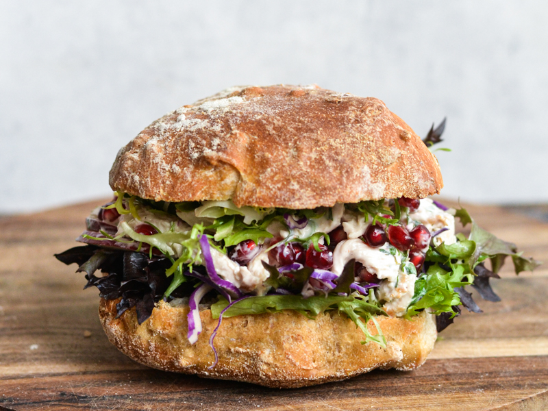 Sandwich med grøntsager, brød og granatæblekerner på træbord