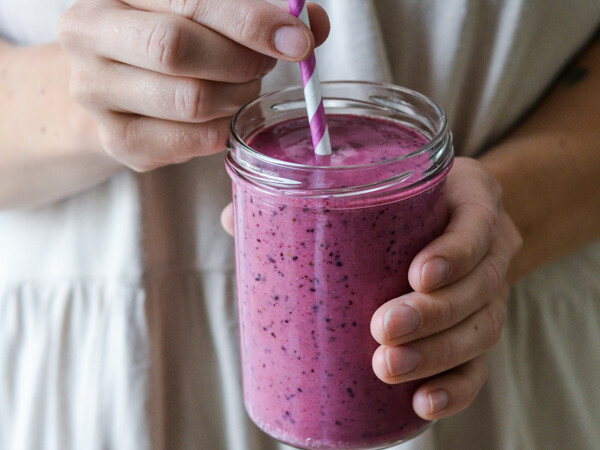 Person holder et glas med lyserød bærsmoothie og sugerør