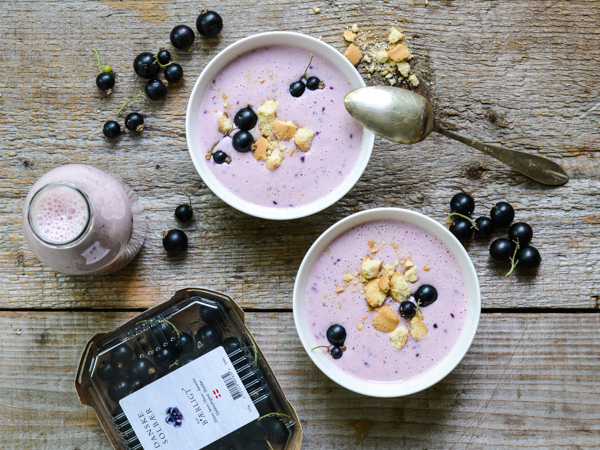 To skåle med purpurfarvet smoothie, drysset med bær og kiks, ved siden af en flaske og solbær.