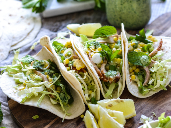 Tre tacos fyldt med kylling, kål, majs og grøn dressing på en træplade