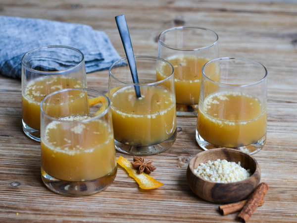 Glas med varm gul drik, omringet af krydderier og en skål
