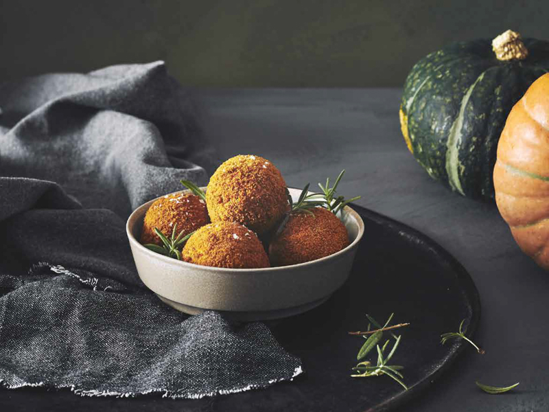 Skål med sprøde græskarboller og frisk rosmarin mod mørk baggrund