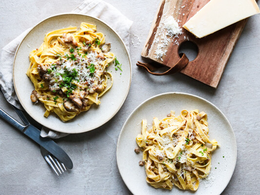 To tallerkener med pasta toppet med svampe og revet ost.