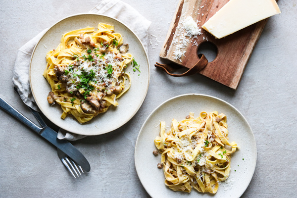 To tallerkener med pasta toppet med svampe og revet ost.