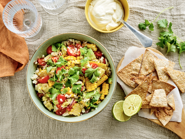 Salat med majskolber, tomater og koriander ved siden af lime og chips