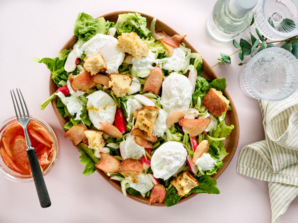 Salat med mozzarella, æbler og brødcroutoner, serveret med dressing og bestik.