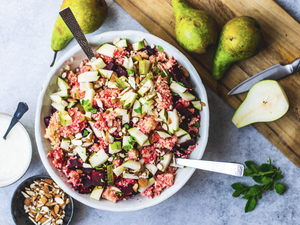 Hvid skål med salat af pærer, rødbeder og nødder på et bord