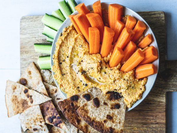 Skål med gulerødder, hummus og brød på et skærebræt