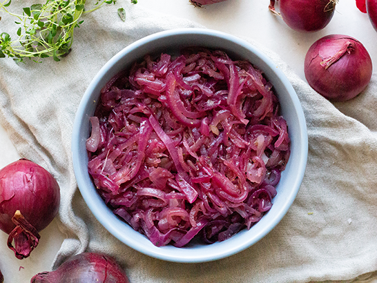 Skål med syltede rødløg omgivet af friske rødløg og krydderurter