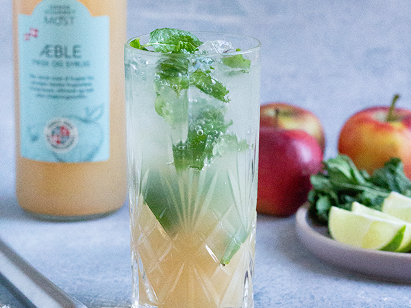 Glas med æblemost, mynte og lime foran æbler og urter