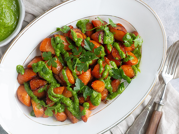 Bagte gulerødder toppet med grøn sauce og krydderurter på et fad