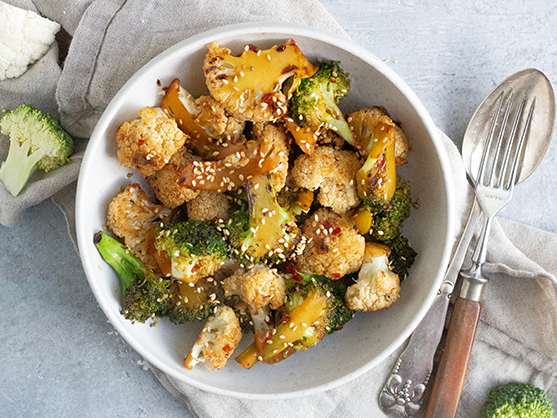 En skål med ristet broccoli og blomkål toppet med sesamfrø