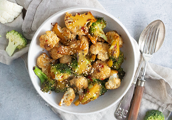 En skål med ristet broccoli og blomkål toppet med sesamfrø