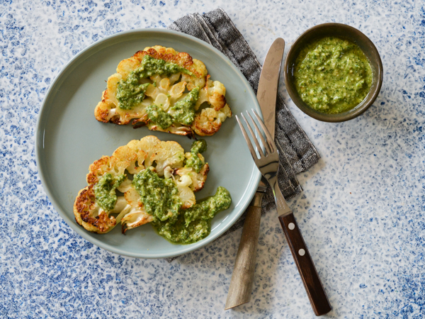 Grillede blomkålsskiver serveret på en tallerken med grøn pesto
