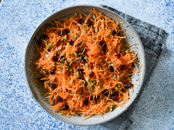 Gulerødder, kerner og tranebær i en skål på blå bord