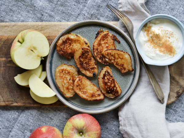 Æbleskiver på en tallerken med æblestykker og creme ved siden af.