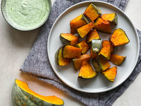 Tallerken med ristede græskarstykker ved siden af grøn dip og stofserviet.