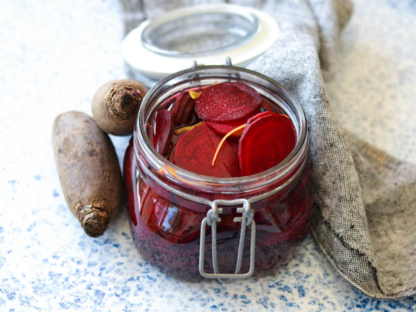 Et åbent glas med syltede rødbeder ved siden af friske rødbeder på en bordplade