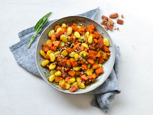 En skål med gnocchi, græskar og pekannødder på en stofserviet.