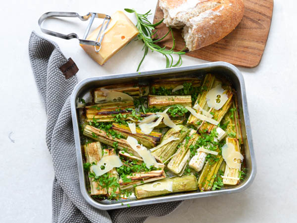 Ovnbagte porrer i fad toppet med ost og urter, ved siden af brød