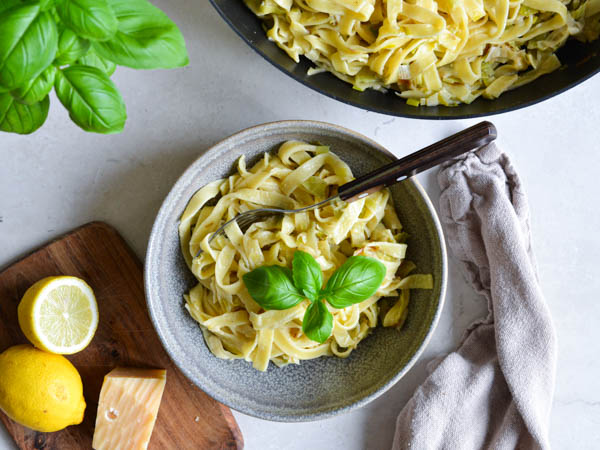 Skål med frisk pasta toppet med basilikum, omgivet af citroner og ost.