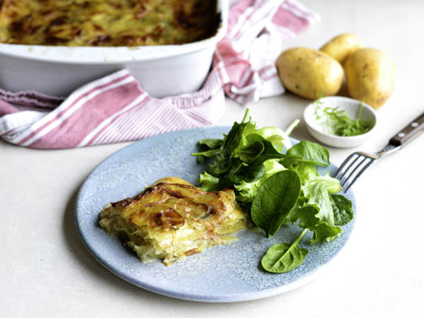 Kartoffelgratin serveret med frisk grøn salat på en tallerken ved siden af et fad.