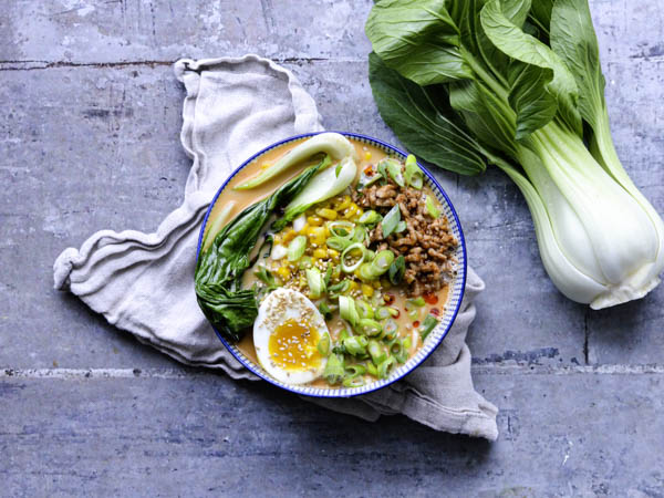 Ramen i en skål med bok choy og et kogt æg ved siden af på stofserviet